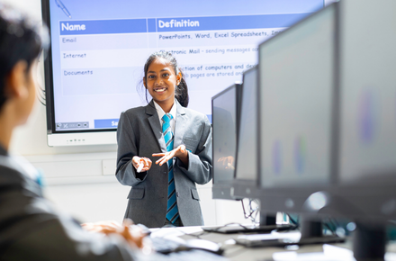 Girl stood infront of a whiteboard with rows of computers infront