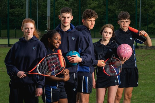 Students posing in PE uniform with sports equipment