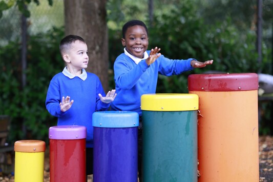 Monkwick Infant and Nursery School - Pupils playing special drums outdoors in uniform